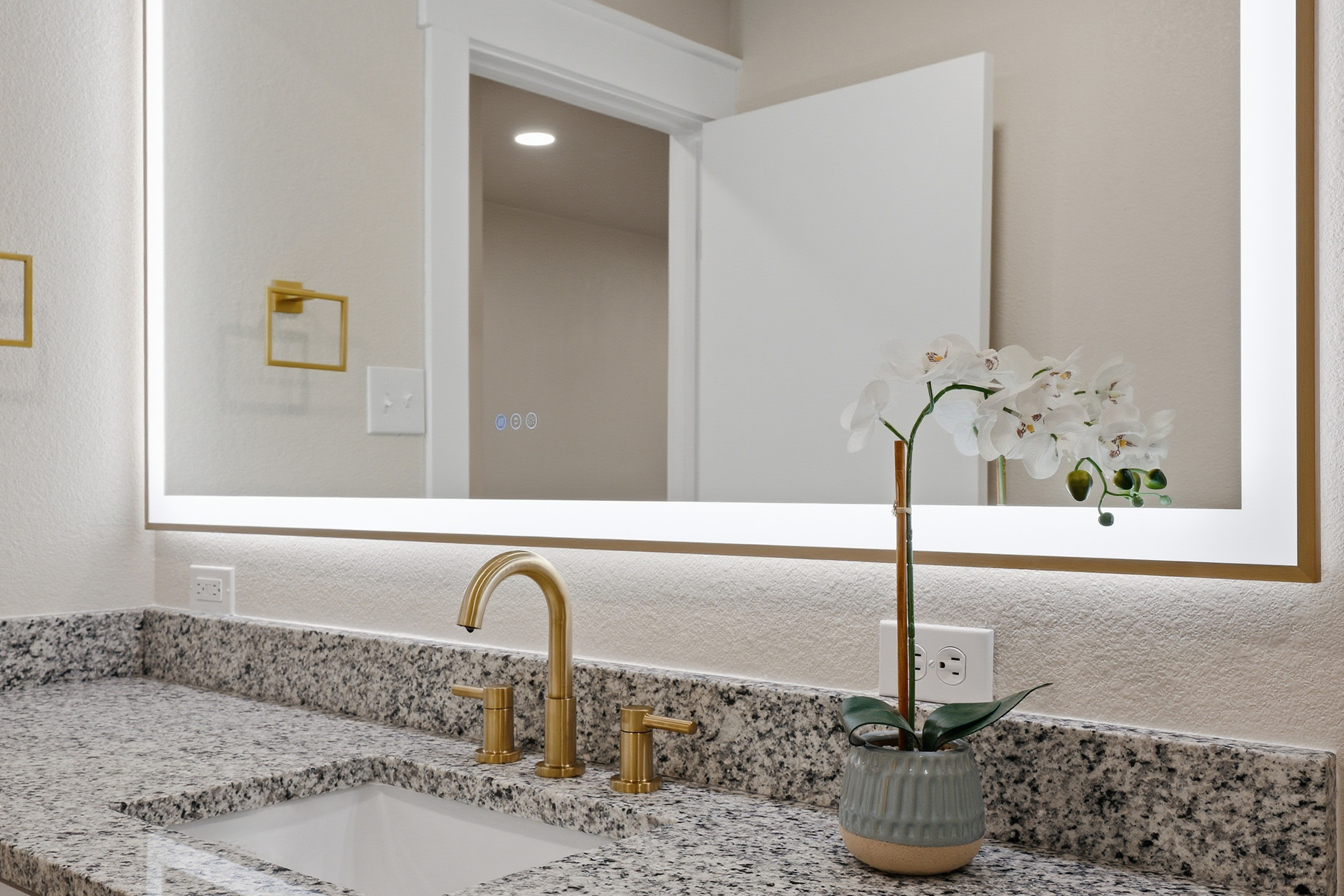 Master bathroom close-up of LED mirror, gold faucet, granite countertop, and undermount sink